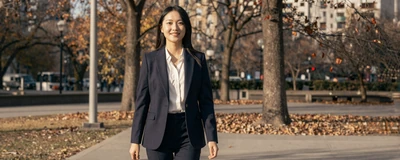 Female respiratory therapist walking through a sunlit autumn park in a navy blazer