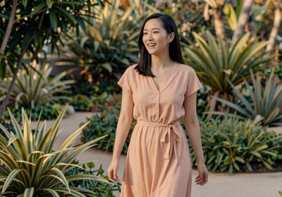 Woman walking joyfully through a sunlit botanical garden in a peach dress