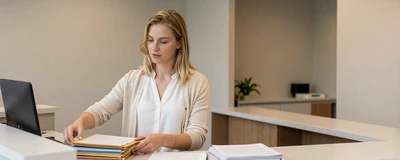 Female medical assistant organizing files at a tidy clinic reception desk