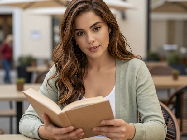 Female pediatrician reading a book at an outdoor café in a sage cardigan