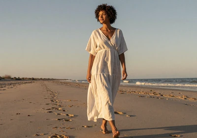 Woman doctor walking on a beach at sunset in a white linen dress